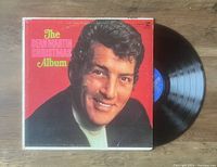 Photo showing Dean Martin's The Christmas Album vinyl LP record partially removed from its sleeve, with cover featuring a close-up portrait of Dean Martin on a red background with yellow and pink text.