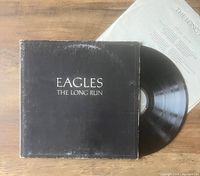 Photo showing black vinyl record partially out of original black cover sleeve with title text