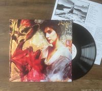 Watermark vinyl LP record partially out of cover with lyric insert above it on wooden surface