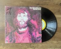 Photo shows the front cover of the Kris Kristofferson Border Lord vinyl LP with pink/red portrait artwork and the vinyl record partially pulled out from the sleeve with visible label.