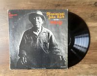 Photo showing front cover of Mississippi John Hurt's 'Today!' vinyl LP album and the black vinyl record partially taken out of the sleeve on a wooden surface.