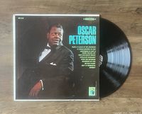 Photo of Oscar Peterson vinyl LP record partially pulled out of its cover featuring artist portrait and track listing.