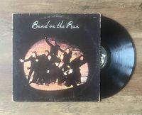 Vinyl record 'Band on the Run' by Paul McCartney with cover art showing multiple men in a spotlight against a brick wall, the record partially pulled from the sleeve.