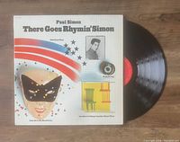 Photo showing front cover of 'There Goes Rhymin' Simon' album and vinyl record partially visible beside it on wooden surface.