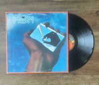 Photo of Prism vinyl LP record next to its front cover with colorful prism artwork and orange border on wooden surface.