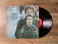 Vinyl record partially removed from original album cover showing image of Simon and Garfunkel and Columbia label on record.