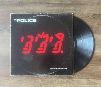 Photo showing The Police 'Ghost In The Machine' vinyl LP partially pulled out of the album cover on a wood surface. The album cover has visible signs of wear and some corner creasing.