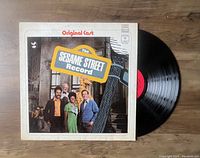 Vinyl LP record partially out of album cover showing original cast of Sesame Street on the front cover with Sesame Street sign and characters.