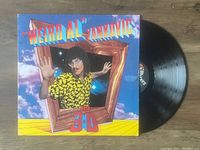 Photo of the Weird Al Yankovic In 3-D vinyl LP record with album cover and black vinyl displayed on a wooden surface.