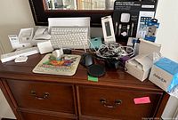Overview of lot on wooden dresser showing keyboards, mice, cables, charging station, adapters, speaker box