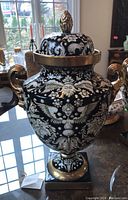 Full view of black ceramic vase with lid, gilt handles and square base