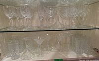 Two glass shelves filled with assorted crystal glassware including stemmed glasses and tumblers.