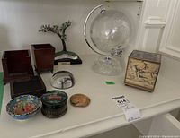 Photo showing the full lot on white shelf including globe, wooden containers, brass box, paperweights, painted bowl, and decorative items