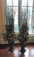 Front view of both urn planters with full faux floral arrangements against window