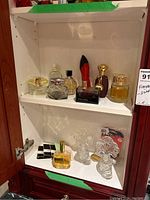 Two white shelves containing assorted perfume bottles, boxes, and decanters