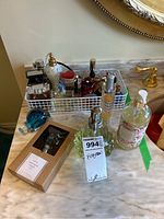 Overview of multiple fragrance and perfume bottles displayed in white wire basket on marble surface, plus two hand soap bottles and boxed perfume on the marble counter.
