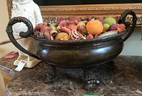 Overall view of brass-tone bowl filled with faux fruits on marble surface