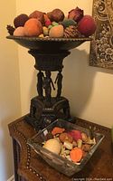 Overview of bronze-style centrepiece bowl filled with faux fruit and Vidivi glass bowl with potpourri on wood table