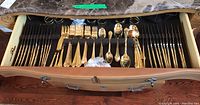 Full drawer showing rows of gold-tone forks, knives, spoons and stacked napkin rings