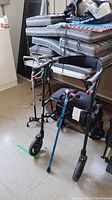 Wide view of all four mobility aids including rollator walker and three canes leaning against stacked cushions