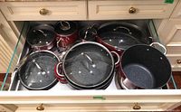 Drawer shot showing red Curtis Stone pots and pans stacked with lids