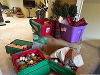 Five storage bins (not included) filled with ornaments, two faux berry cone trees, and a holiday cushion on top of a large tree box