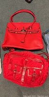 Top-down view showing large red structured satchel, red messenger-style bag and partial wallet