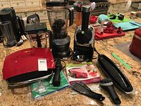 Photo showing Yonanas frozen fruit dessert maker, Nutribullet blender, Broil countertop grill, manual, small black spatula, black cleaning brush, tamper tool, and green placemats.