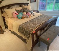 Bed with beige quilted comforter, three matching pillow shams, two damask decorative pillows and assorted Squishmallow plush pillows arranged on top