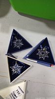Three triangular boxes each containing a Swarovski crystal star ornament.