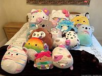 Photo showing 14 assorted Squishmallows plush toys arranged on a bed, featuring various characters and colors.