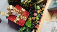 Two glitter gift box decorations (red and green) next to artificial garland.