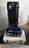 Black Golf Guard hard sided golf travel case, white Yeti cooler and two foldable picnic baskets in garage.