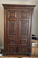 Full front view of brown stained hardwood armoire with raised panels and fretwork doors