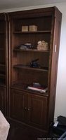 Front view of dark brown wooden bookcase with three shelves and bottom cabinet