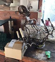 Bronze toned metal chandelier seen from a side angle with floral and glass crystal accents, positioned on a workbench next to a box containing spare bulbs.