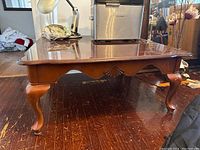 Side view showing wood coffee table with curved legs, carved apron with shell motif and inlay top.