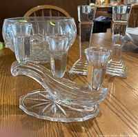 Photo showing all three crystal items on a wooden table: two candle holders and a decorative crystal bowl in background. Stickers indicating Hungarian and German origin visible on some pieces.