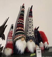 Photo showing six Christmas themed doorstop gnomes with tall patterned knitted hats in holiday colors, white faux fur beards, and wooden noses.