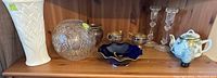 Shelf with white Kaiser bisque vase, clear cut glass bowl/vase, blue JL Meneau dish, silverplate cream and sugar set, hand-painted Japanese teapot, and pair of glass candlesticks.
