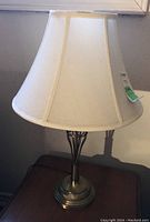Lamp with brass base and beige bell-shaped shade, approx 23 inches tall