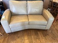 Full front view of grey leather loveseat on wooden floor showing seating and back cushions, and broad padded arms.