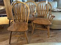 Set of four oak dining chairs including one captain's chair with armrests and three side chairs with spindle backs.