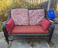 Front view of outdoor loveseat with cushions installed, showing floral patterned and solid red cushions.
