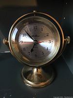 Front view of brass nautical desk clock showing dial with Seth Thomas branding, 12 and 24 hour format, black hour and minute hands, red second hand.