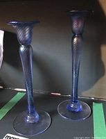 Two blue iridescent art glass candle holders, one taller, one shorter, with spiral patterns and round clear bases.