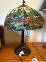 Side view of the stained glass table lamp showing dragonfly motif and metal base with wrapped cord.