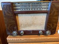 Front view of vintage Philips radio showing wood grain finish, woven speaker cloth, AM band tuning scale, and four control knobs.
