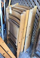 Side view of stacked oak wood folding chairs showing curved back supports and slat seats.