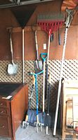 Wide view of all yard tools hanging showing shovels, rakes, garden claw, pole saw